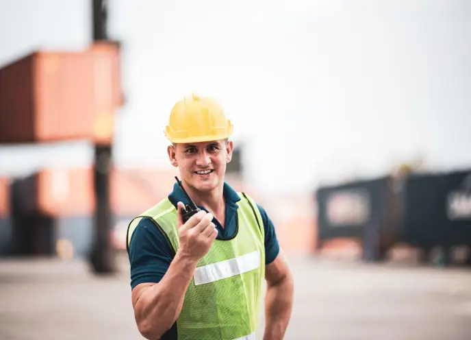 Hamnarbetare med skyddshjälm och reflexväst kommunicerar via walkie-talkie på containerterminal